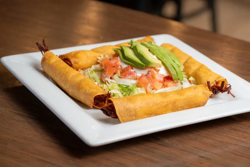 Flautas topped with avocado, pico and crema