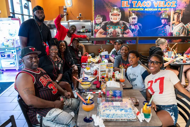 Friends around a table in front of the El Taco Veloz mural