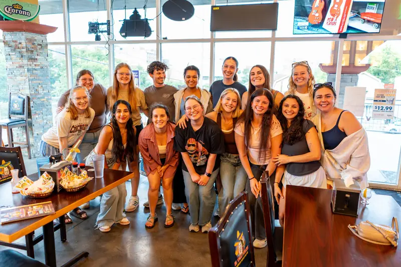 A big group of friends, one in a University of Cincinnati shirt, posing inside El Taco Veloz